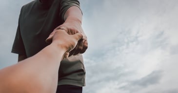 Outstretched hand reaching to hold the hand of a person below