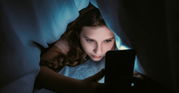 young girl under covers facing tablet blue screen