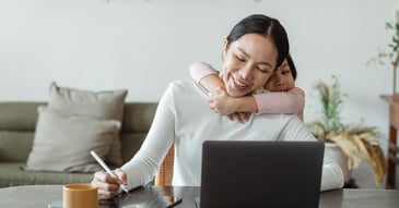 woman at computer with child's arms wrapped around her lovingly