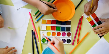 young girls' hands dipping brushes in paint during expressive therapy workshop