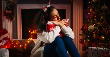 woman in holiday attire hugging red pillow in front of fireplace