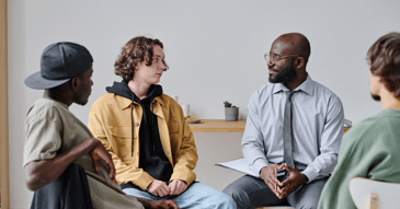 Men's therapy group with young adult male chatting with older man in tie