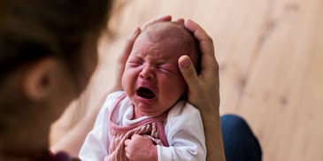 Newborn crying in parent's gentle hands