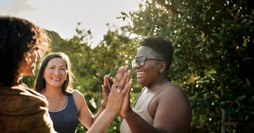 Diverse group of women smiling outdoors and clasping hands