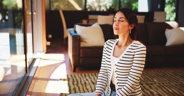 woman facing sunny window, practicing deep breaths