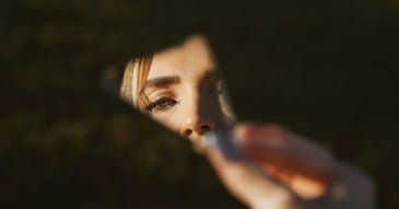 woman looking at herself in broken mirror shard