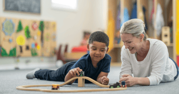 Child on floor playing with blocks while adult female observes. 