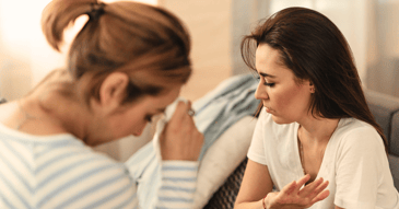 two women sitting close but facing away from each other 