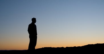 thoughtful man standing alone facing sunset