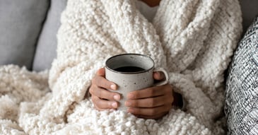 close up hands holding coffee wrapped in layers of blankets