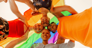 Huddled group of friends under rainbow flag
